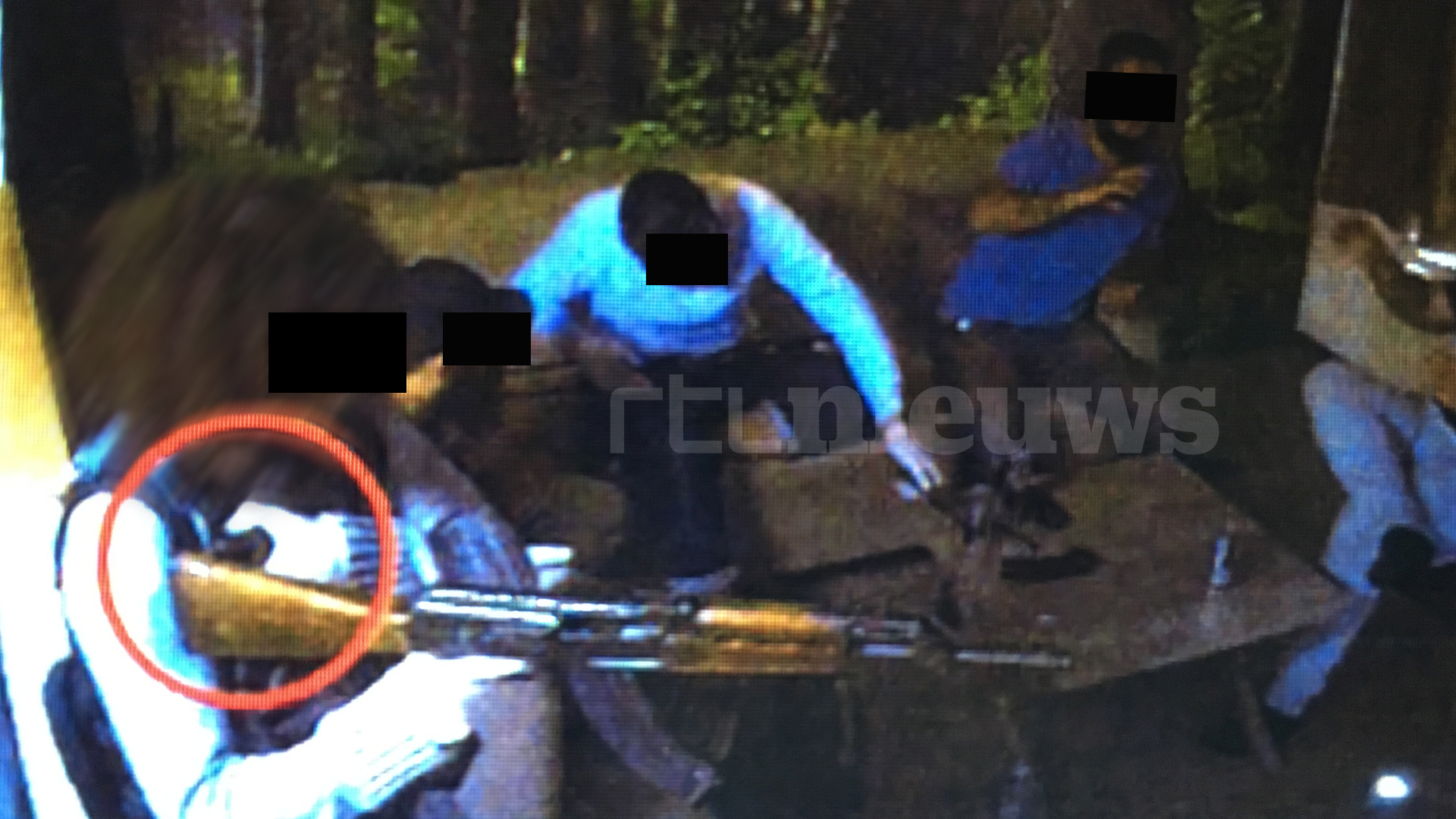 Een verdachte richt zijn kalsjnikov en houdt zijn linkerhand op de ontsteking van zijn bomvest.