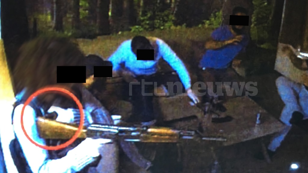 Een van de verdachten draagt een bomvest en houdt een kalasjnikov vast. Met de linkerhand drukt hij op het ontstekingsmechanisme van het bomvest.