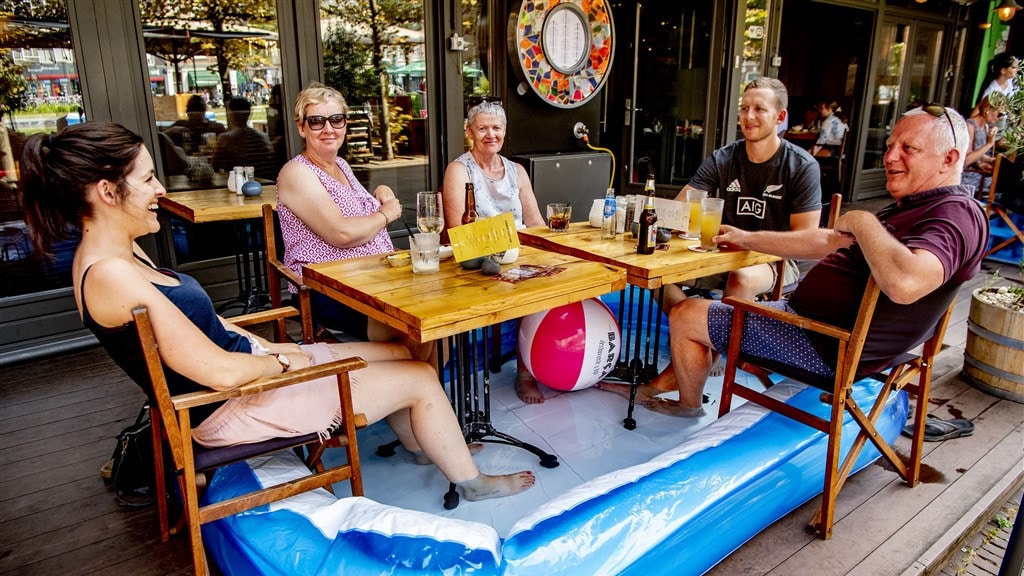 Toeristen zitten op een terras met hun voeten in een opblaaszwembad dat is neergezet wegens de hitte.