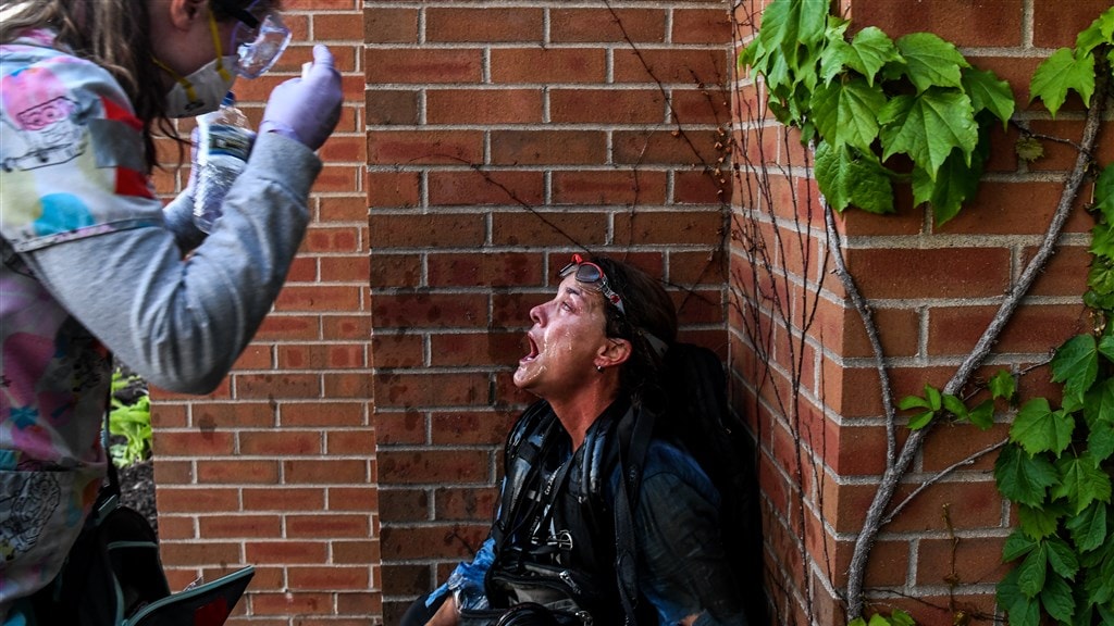 Een demonstrant helpt een journalist die is geraakt door pepperspray.