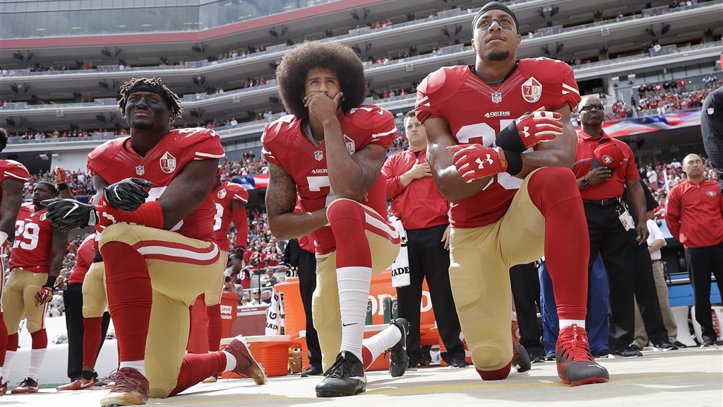 Colin Kaepernick en twee andere American footballspelers knielen tijdens volkslied in 2016.