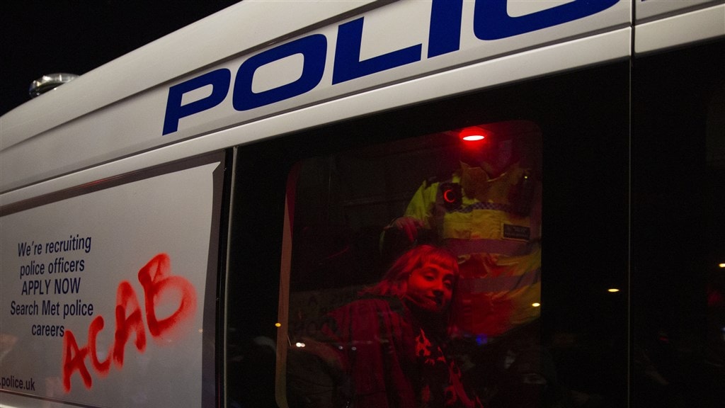 Een gearresteerde vrouw in een politiebus.