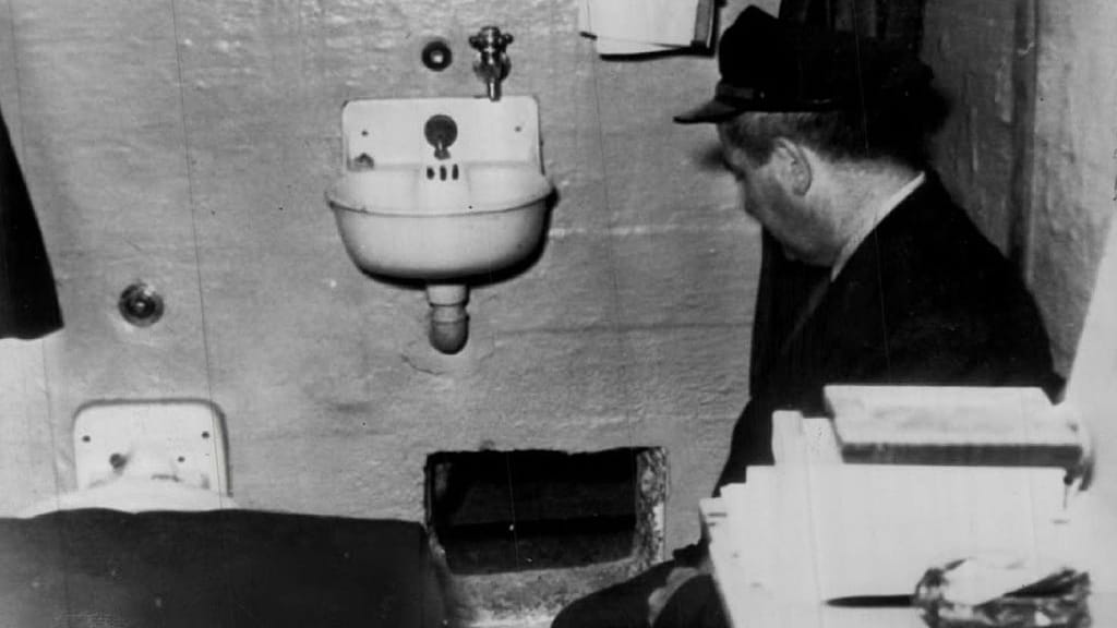 Een bewaker knielt bij het gat in de cel van Frank Morris waardoor hij is ontsnapt.