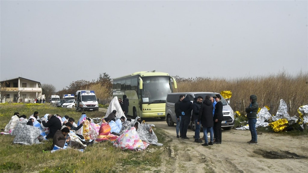 Overlevenden zitten gewikkeld in dekens nabij het strand van Cutro
