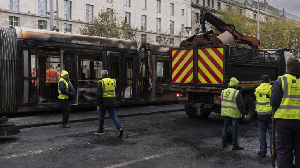 Een uitgebrande tram wordt opgeruimd.