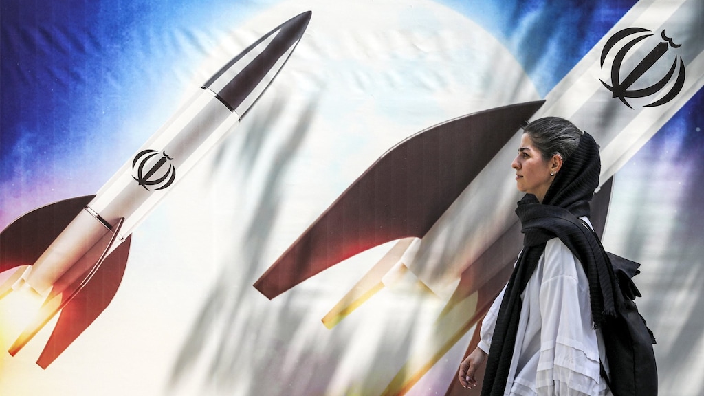 Een Iraanse vrouw loopt langs een banner met raketten, als waarschuwing naar Israël om niet met een tegenaanval te komen.