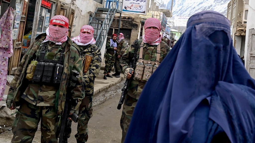 Een gesluierde vrouw loopt langs talibanstrijders.