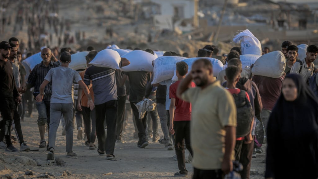 Palestijnen in de Gazastrook dragen voedselpaketten van de GHF op hun rug in het noorden van Gaza-stad.