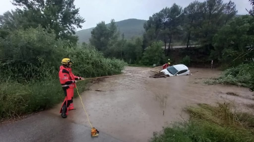 Een brandweerman in Catalonië probeert een auto los te trekken nadat die door het water is meegevoerd.