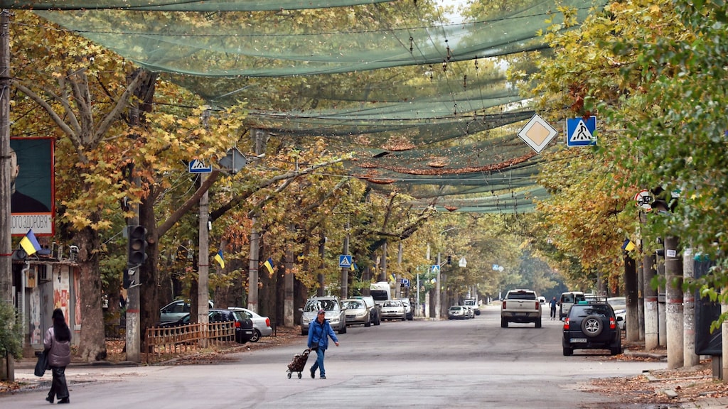 Mensen steken in Cherson de straat over. De netten beschermen hen tegen droneaanvallen.