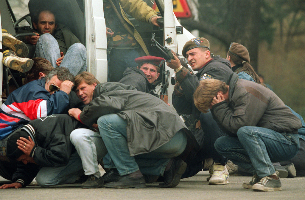 Deze foto, genomen op 6 april 1992, toont een Bosnische soldaat van de speciale troepen (3R) die terugschiet in het centrum van Sarajevo, terwijl burgers proberen te schuilen in een voertuig. 