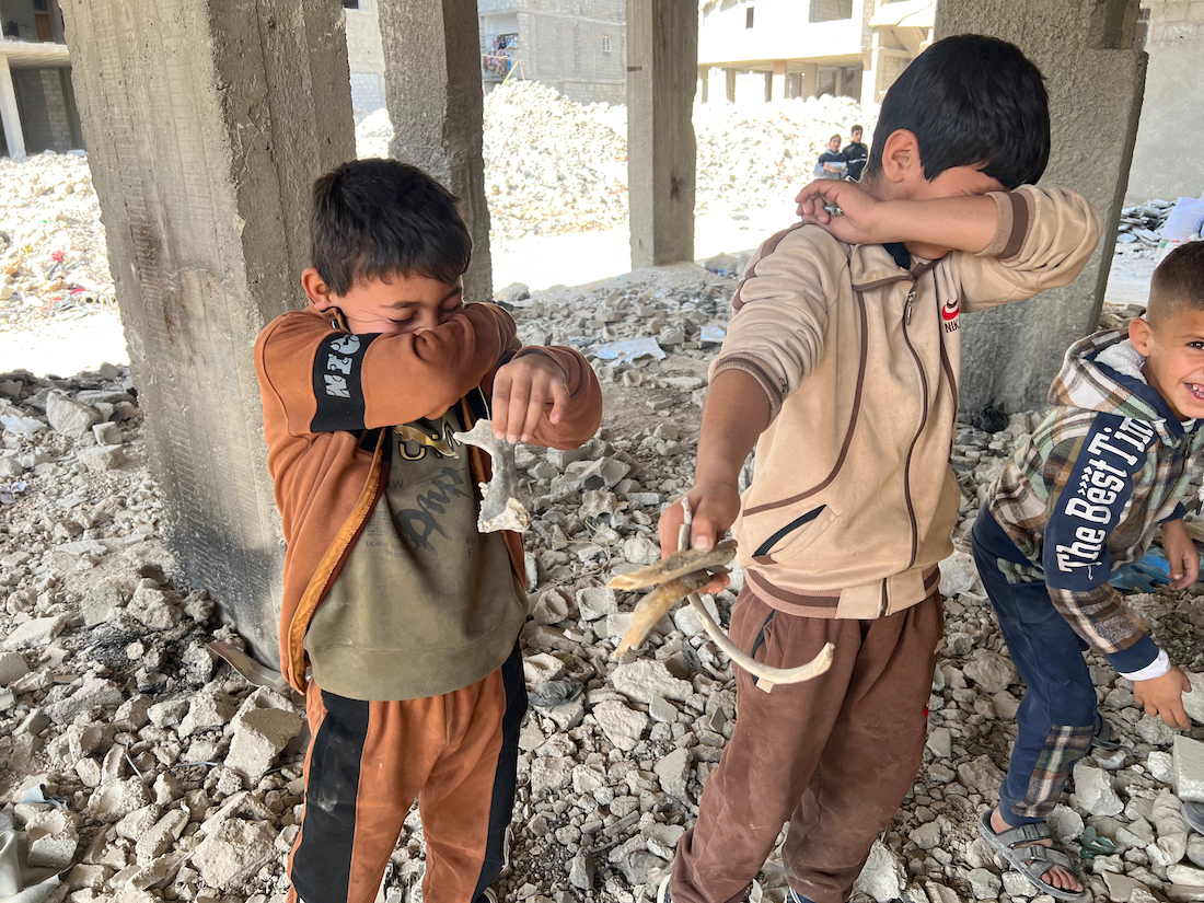 De muffe geur bij de botresten dringt door, lokale kinderen doen hun handen voor hun neus